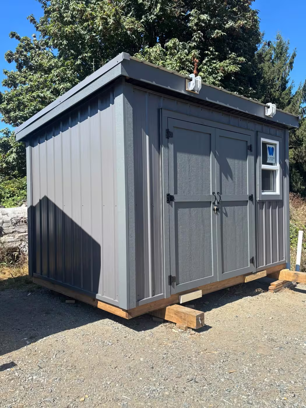 Dark grey metal shed with double doors and a window, with white lifting lugs on the roof